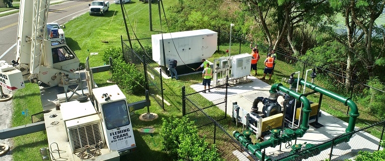 Work crews secure a large generator unit from a crane