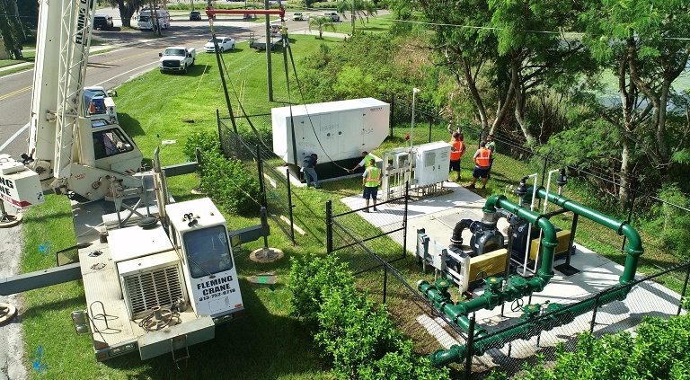 Work crews secure a large generator unit from a crane